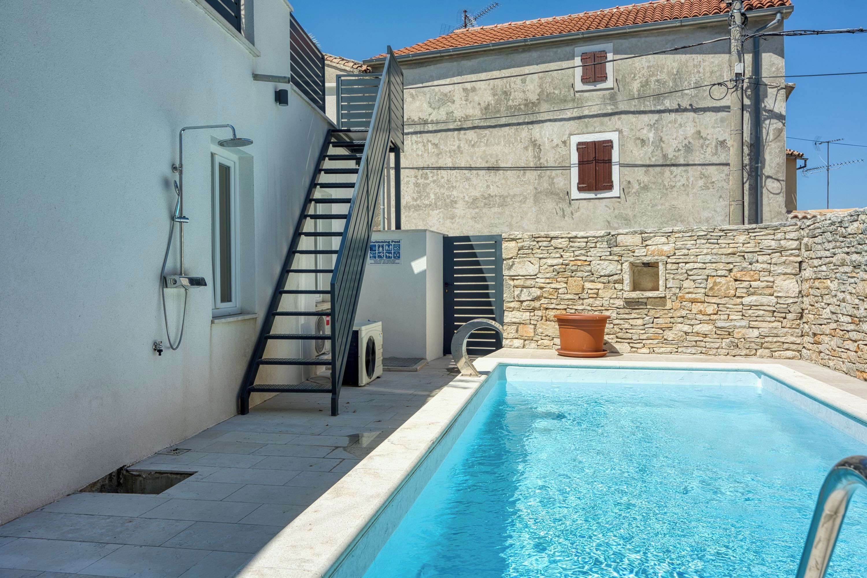 Una piscina junto a un edificio con pared de piedra, una escalera y una puerta.