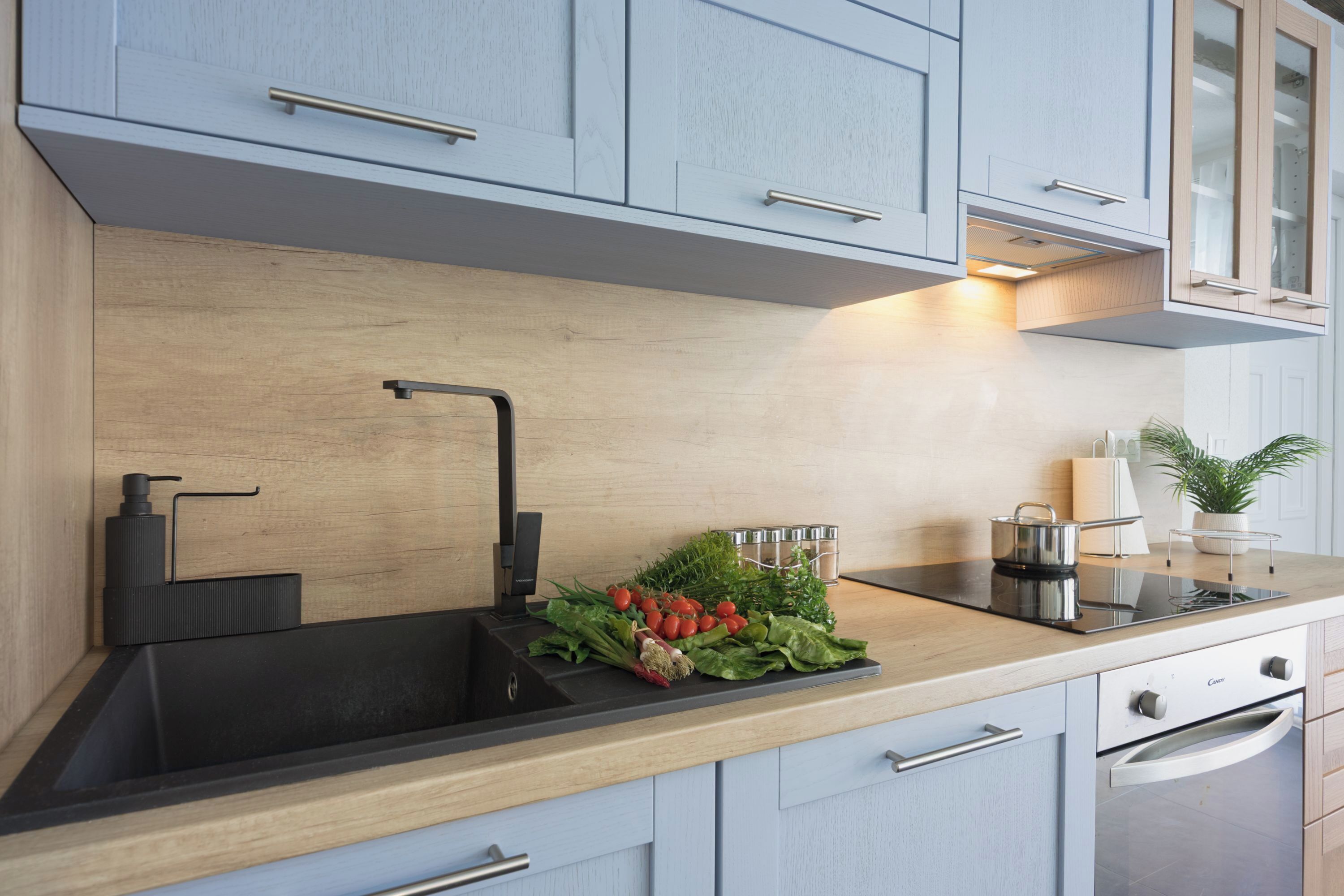 A modern kitchen with a black sink, wooden countertop, and light blue cabinets.