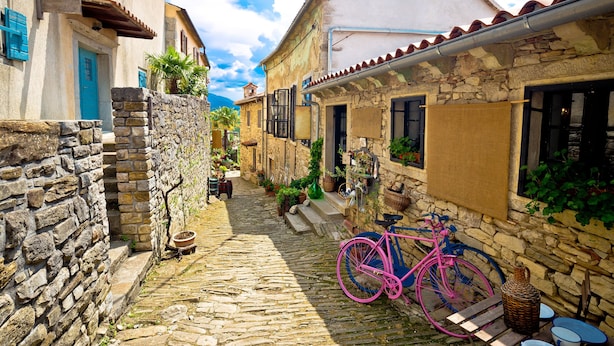 A narrow cobblestone street with stone buildings, a pink bicycle, and outdoor seating. - Stone Villa Galant with Pool (Lanisce)