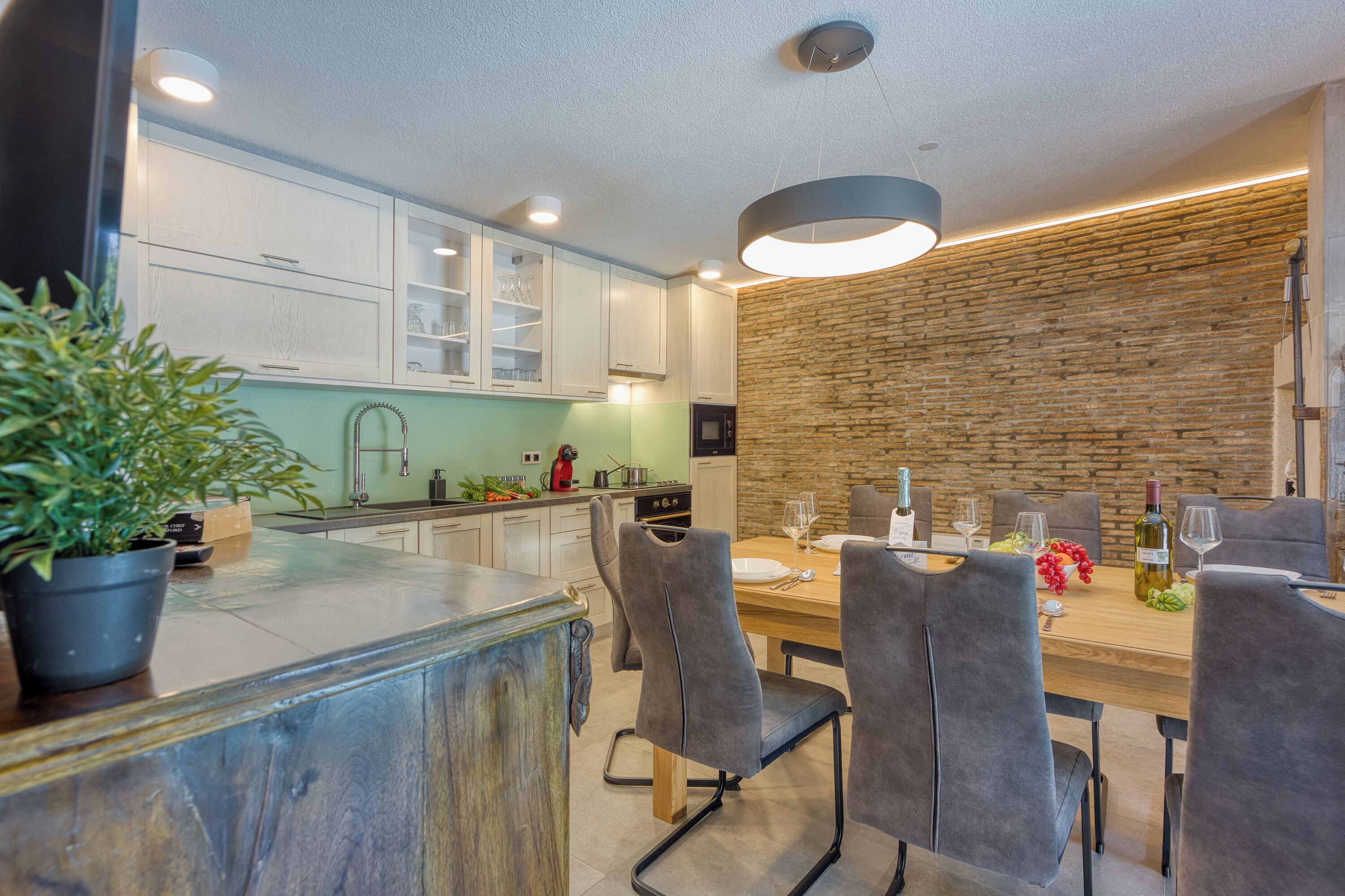 A modern kitchen with white cabinets, a wooden island, and a dining area with grey chairs and a wooden table.