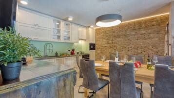 A modern kitchen with white cabinets, a wooden island, and a dining area with grey chairs and a wooden table.