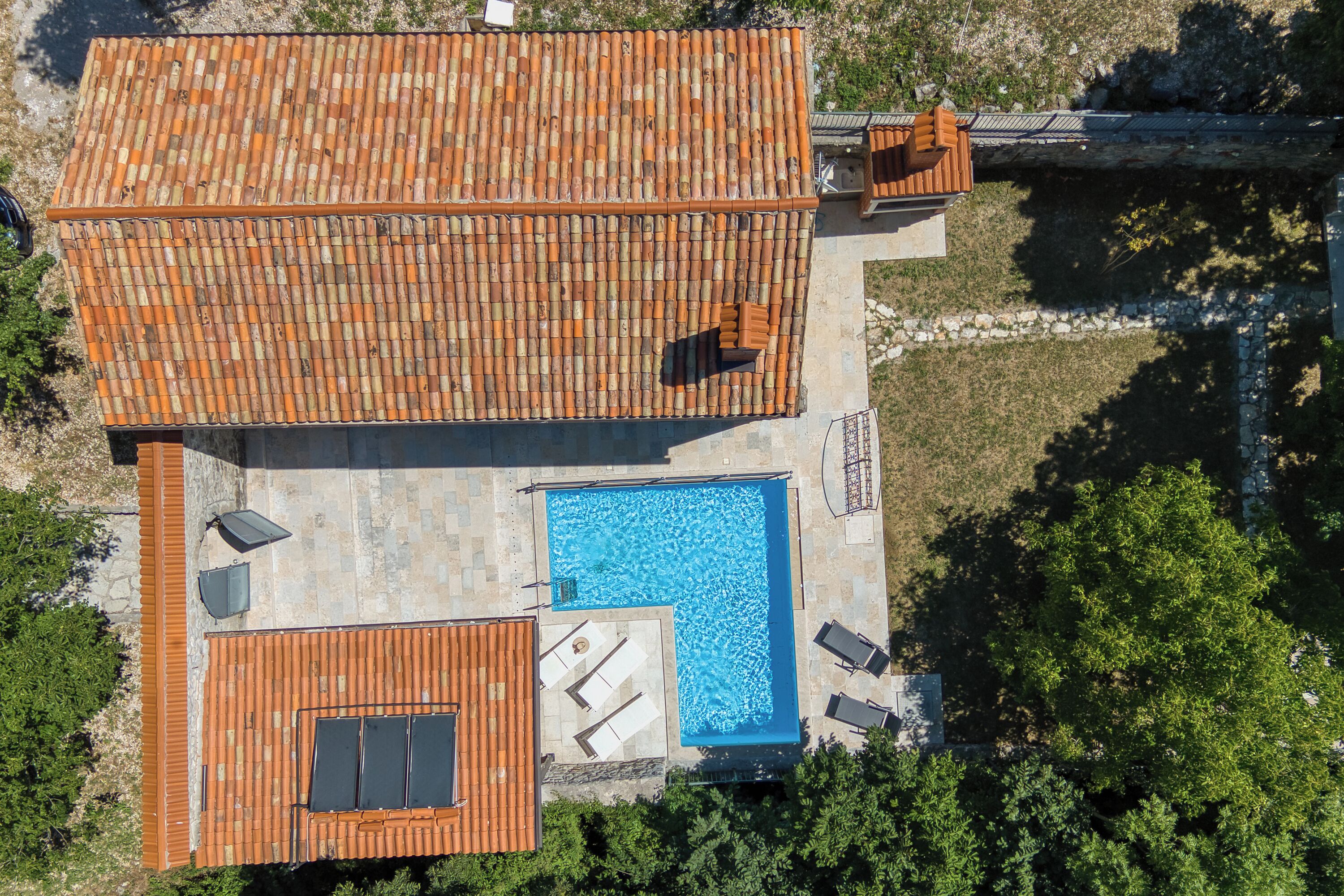 An aerial view of a property with a swimming pool, a covered patio area, and a tiled roof.