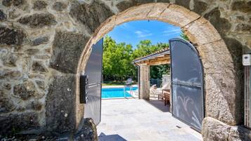 An outdoor swimming pool area with stone walls and a pergola.