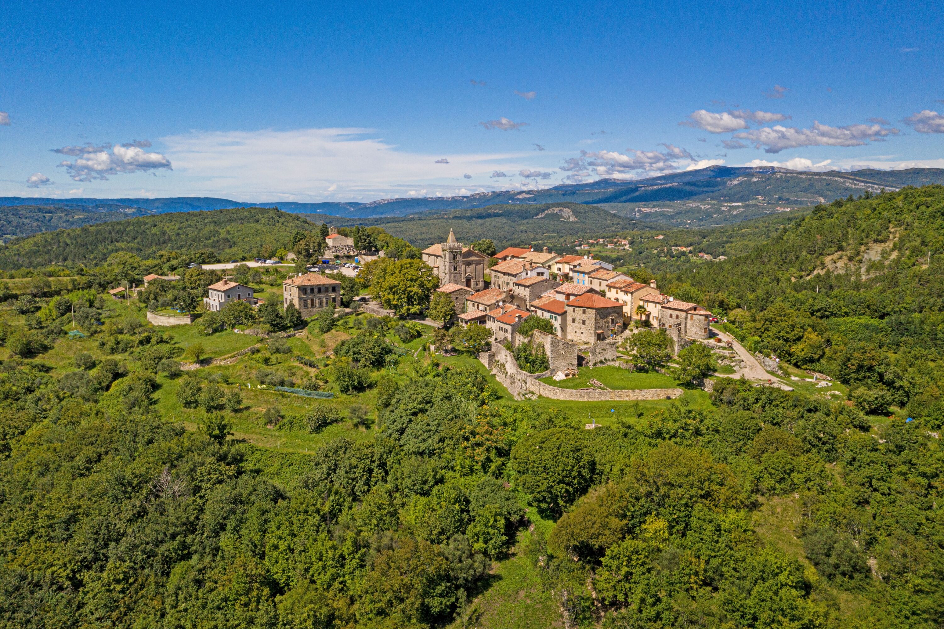Une ville chargée d’histoire, avec une église centrale entourée de bâtiments traditionnels, située dans un paysage verdoyant et vallonné.