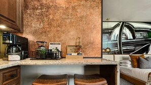 Une cuisine moderne équipée d’une machine à café, d’un moulin à café et d’une pancarte sur laquelle on peut lire : « deux feuilles et un bourgeon ». Il y a deux tabourets devant le comptoir.