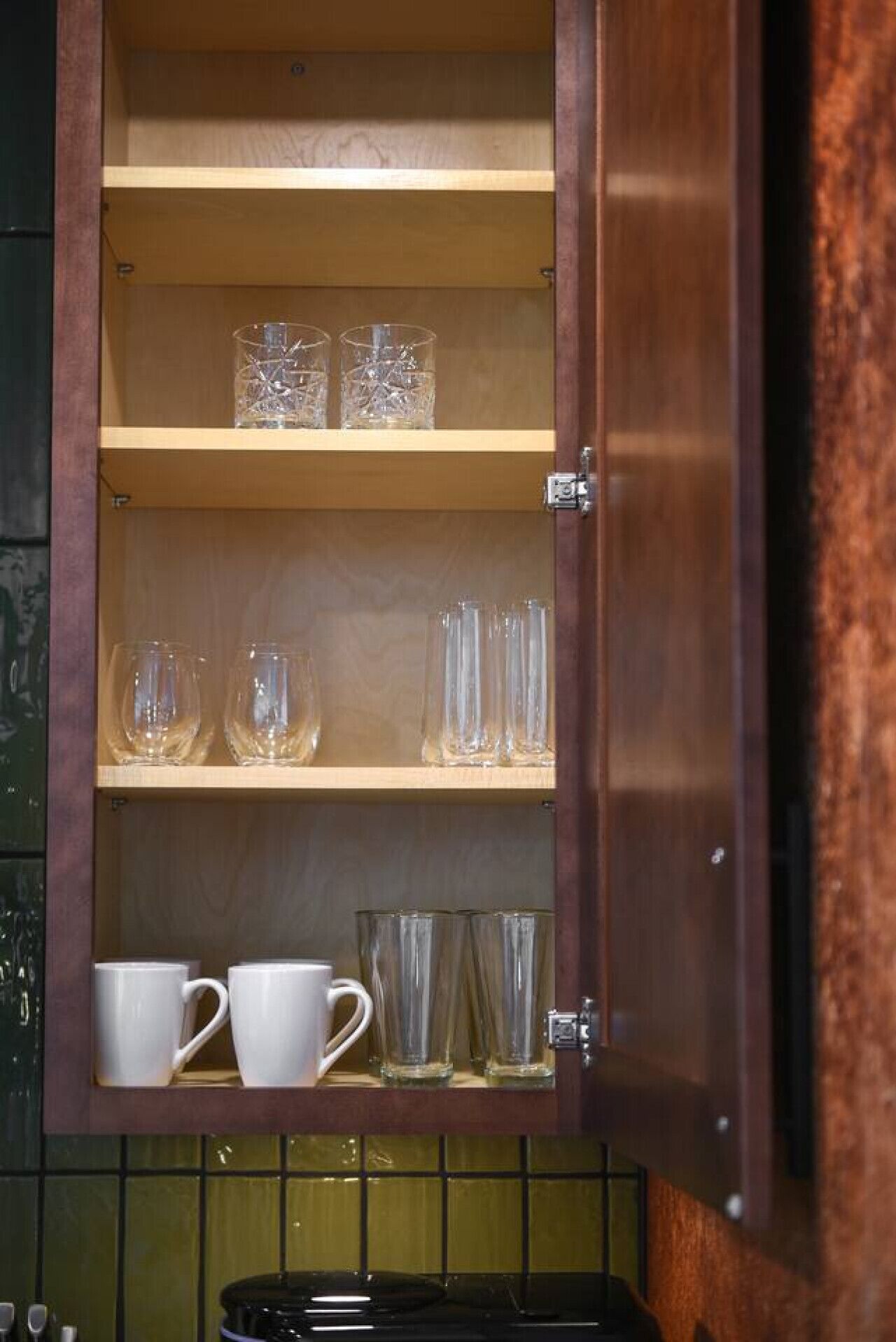 Een houten kast met meerdere planken, waarvan sommige helder glaswerk en witte keramische mokken bevatten.
