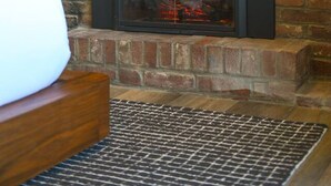 Une cheminée avec un mur en briques, un banc en bois et un tapis à motifs.