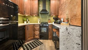 Une cuisine avec des meubles en bois, un réfrigérateur noir, une cuisinière et un plan de travail en marbre.