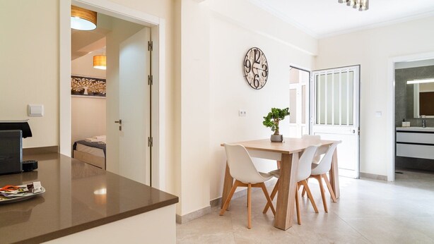 A modern kitchen with a dining area, a clock on the wall, and a potted plant.