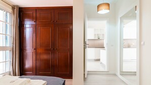 A bedroom with a large wooden wardrobe, a bed with a grey quilt, and a window with curtains.