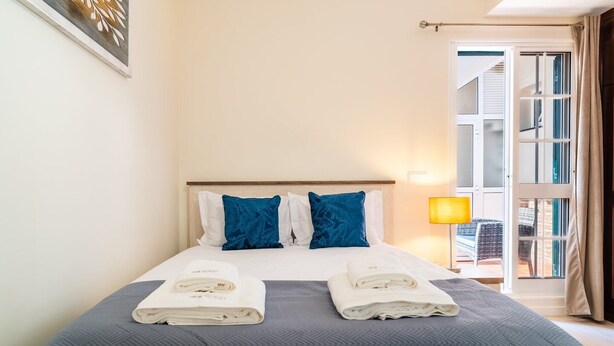 A hotel room with a bed, two pillows, a bedside lamp, and a view of the outside.