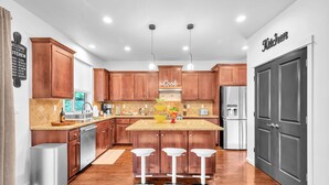 Una cucina moderna con mobili in legno, un'isola centrale con sgabelli, elettrodomestici in acciaio inossidabile e un cartello con la scritta 'Welcome to My Kitchen'.