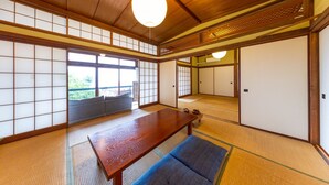 A traditional Japanese room with tatami flooring, a wooden table, sliding doors, and a view of the outdoors. - Azamian Atami (Atami)