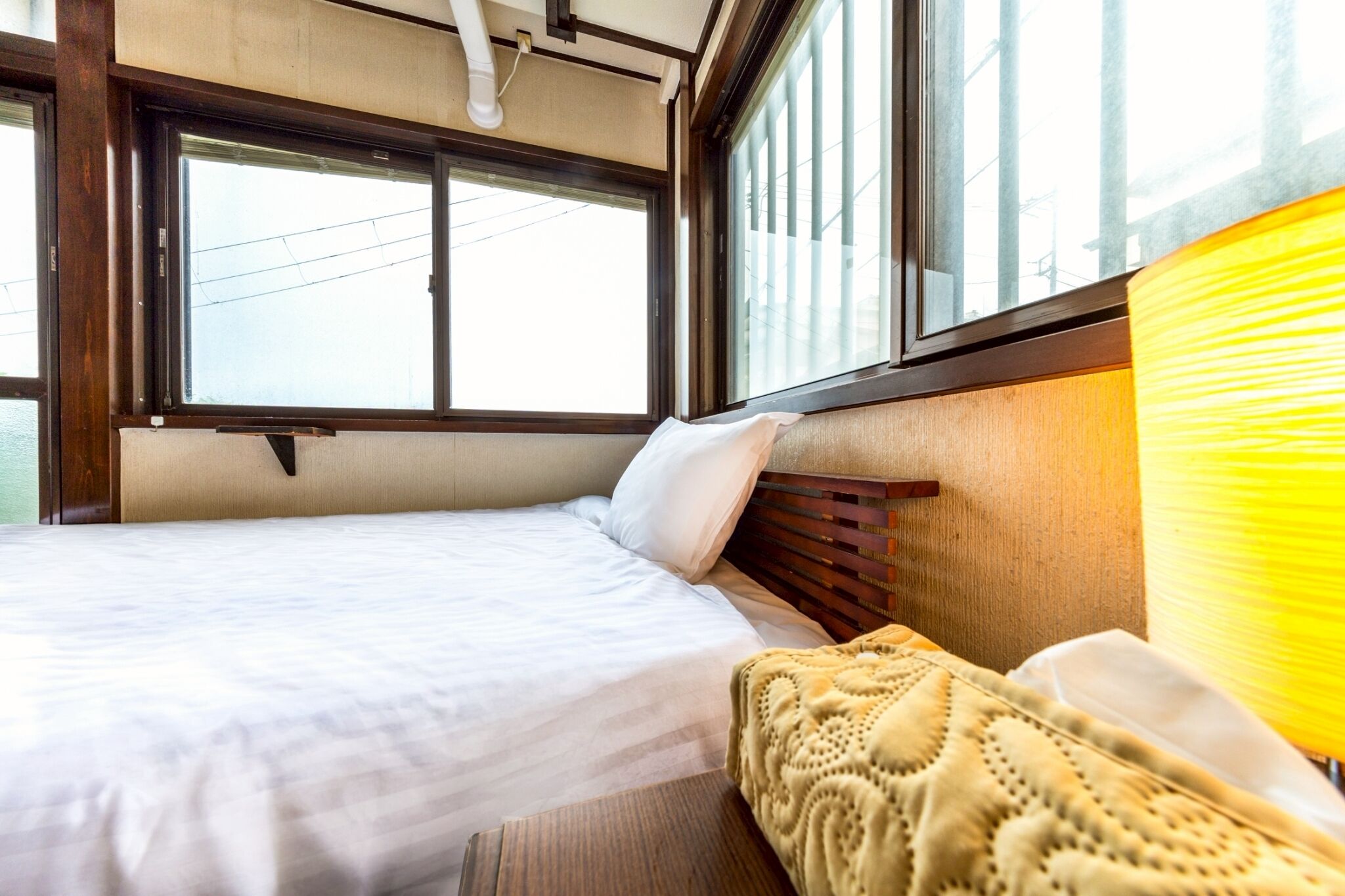 A bed with a wooden headboard, a window with blinds, and a yellow lamp.