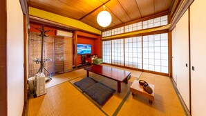 A traditional Japanese room with tatami flooring, a television, a futon bed, and sliding doors. - Azamian Atami (Atami)