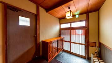 A traditional Japanese interior with a wooden door, sliding shoji screen, tatami flooring, and a low wooden bench.