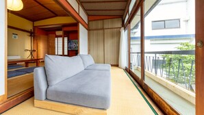 A room with a sofa, tatami flooring, a sliding door, and a view of a building outside. - Azamian Atami (Atami)