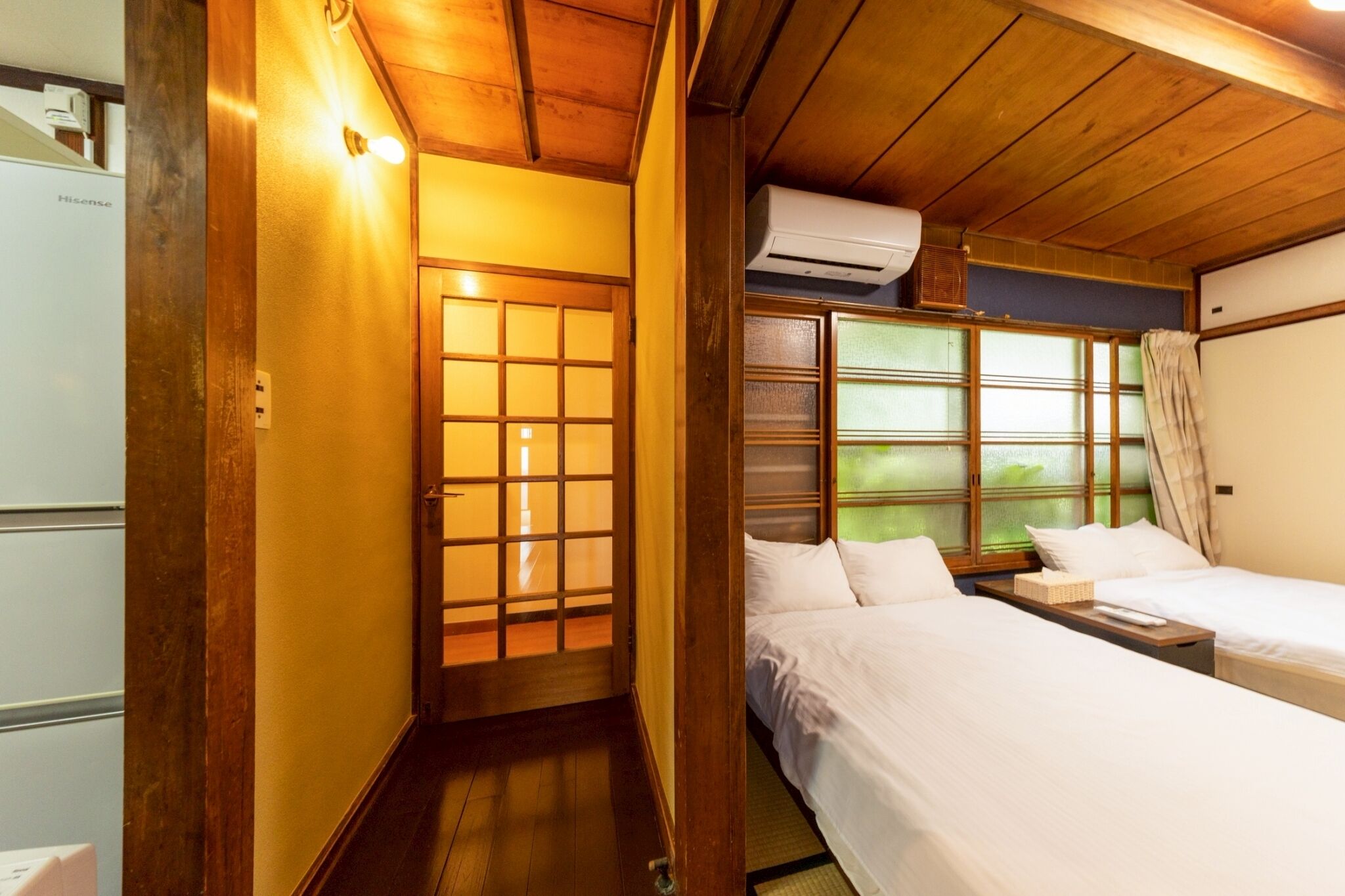 A traditional Japanese-style room with a sliding door, two beds, a small table, and an air conditioning unit.