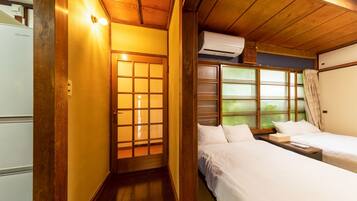 A traditional Japanese-style room with a sliding door, two beds, a small table, and an air conditioning unit.