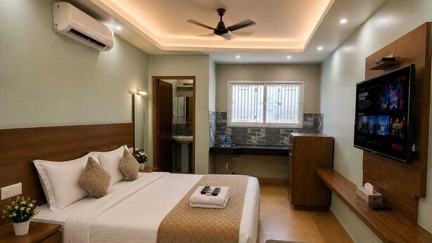 Un dormitorio con cama, mesitas de noche, televisor, ventilador de techo y ventana.