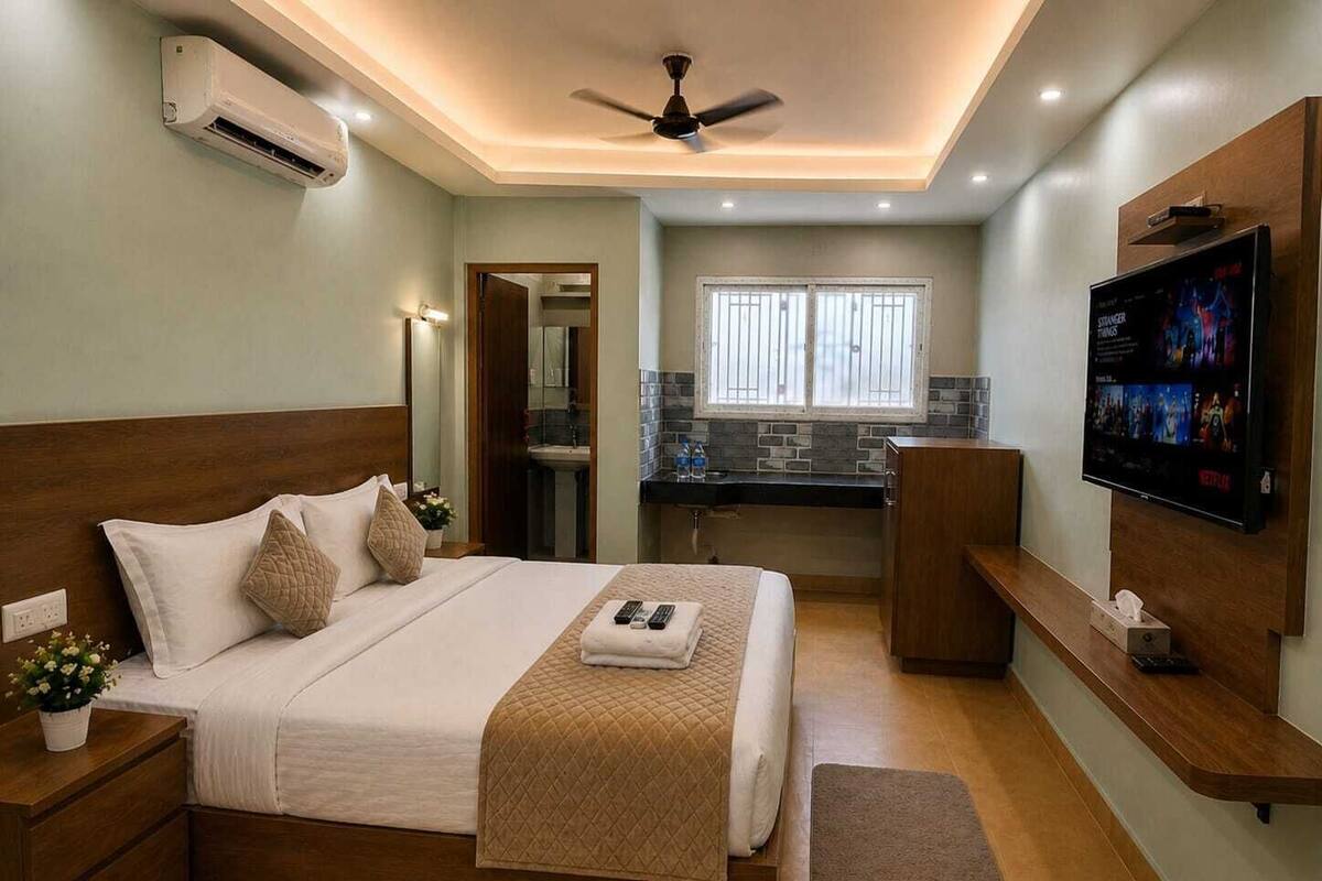 Une chambre à coucher avec un lit, des tables de chevet, une télévision, un ventilateur de plafond et une fenêtre.