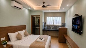 Un dormitorio con cama, mesita de noche, televisor, escritorio y baño visible a través de una puerta abierta.