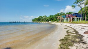 A beach with clear waters, a wooden pier, and colorful houses on stilts.