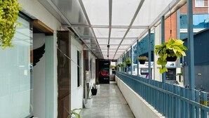 A covered corridor with potted plants, a blue railing, and a clear ceiling. - Wildwings premium hotel (Hyderabad)