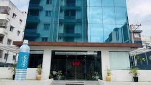 A modern building with a glass facade, a central entrance with a red sign, and a staircase leading up to the entrance. - Wildwings premium hotel (Hyderabad)