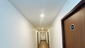 A long, narrow hallway with wooden flooring and white walls. There is a door on the right with a number plate indicating room 507. - Wildwings premium hotel (Hyderabad)