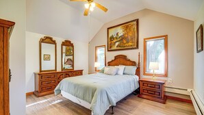 A bedroom with a large bed, wooden headboard, two nightstands, a ceiling fan, and a painting on the wall.