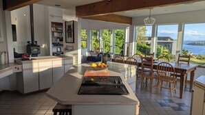 Una cocina moderna con una isla central, un comedor con sillas de madera y grandes ventanales que ofrecen vistas al exterior.