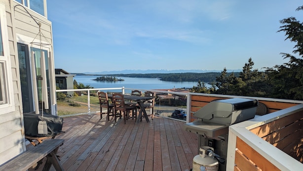 Una terraza de madera con una mesa, sillas, una parrilla y un tanque de propano.