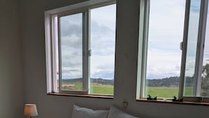 Un dormitorio con cama, dos ventanas, una mesita de noche y una lámpara.