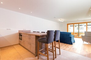 A modern kitchen with a wooden island, bar stools, and a dining area with a blue sofa and a grey armchair. - Vacation apartment living on the Lofer (Reit im Winkl)