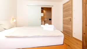Une chambre à coucher avec un lit, une armoire en bois et une salle de bain visible à travers une porte ouverte.