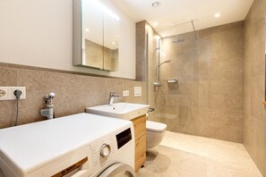 A modern bathroom with a dual sink, a toilet, a shower, and a Bosch washing machine.