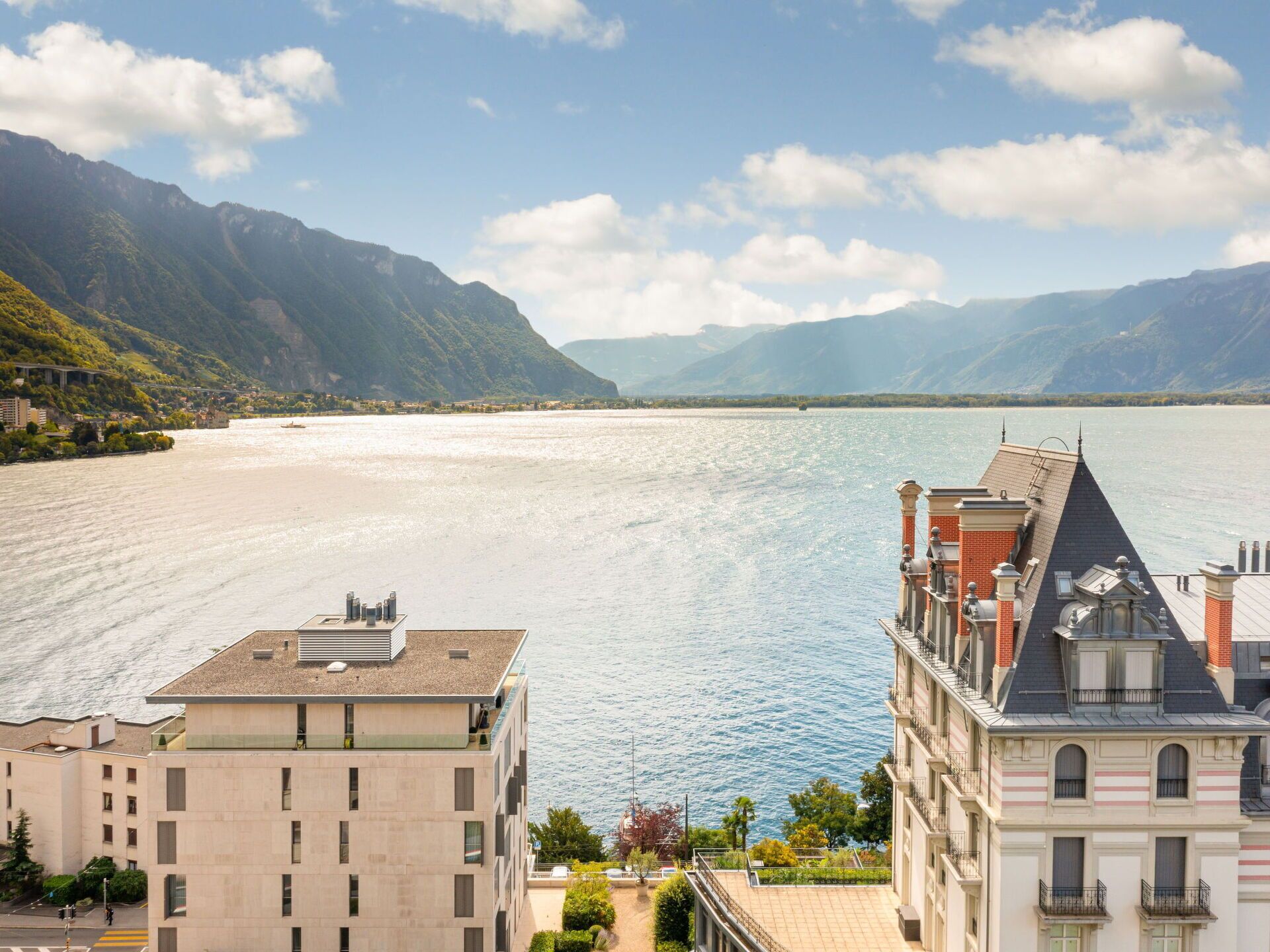 Vue d’un bâtiment situé au bord de l’eau, doté d’un balcon donnant sur un lac paisible, le tout entouré de montagnes.