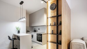 Uma cozinha moderna com uma ilha central, banquetas pretas, uma estante de madeira e um relógio na parede.