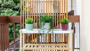 Um banco de madeira com duas plantas em vasos, um em vaso verde e outro em vaso roxo, colocado sobre uma mesa branca.