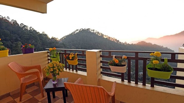 Ein Balkon mit Korbstühlen, einem Tisch und hängenden Blumentöpfen mit gelben Blüten.