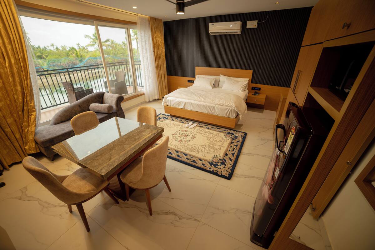 A hotel room with a balcony, a bed, a TV, a dining area with a table and chairs, and a carpet.