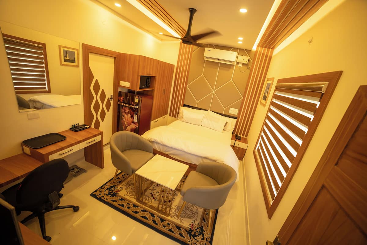 A compact hotel room with a bed, desk, chair, and a ceiling fan.