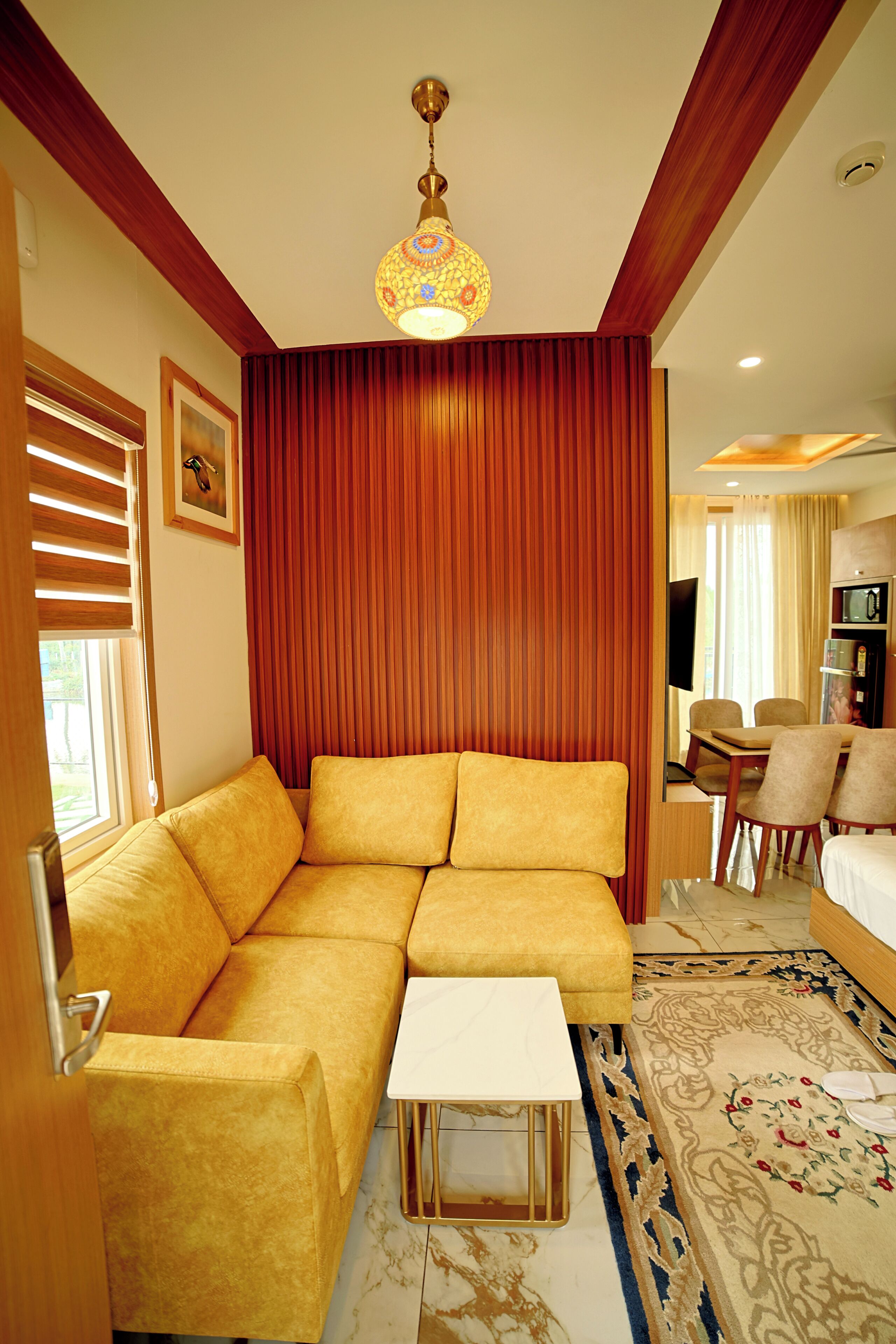 A modern hotel room with a sectional sofa, a small table, a TV, and a dining area.