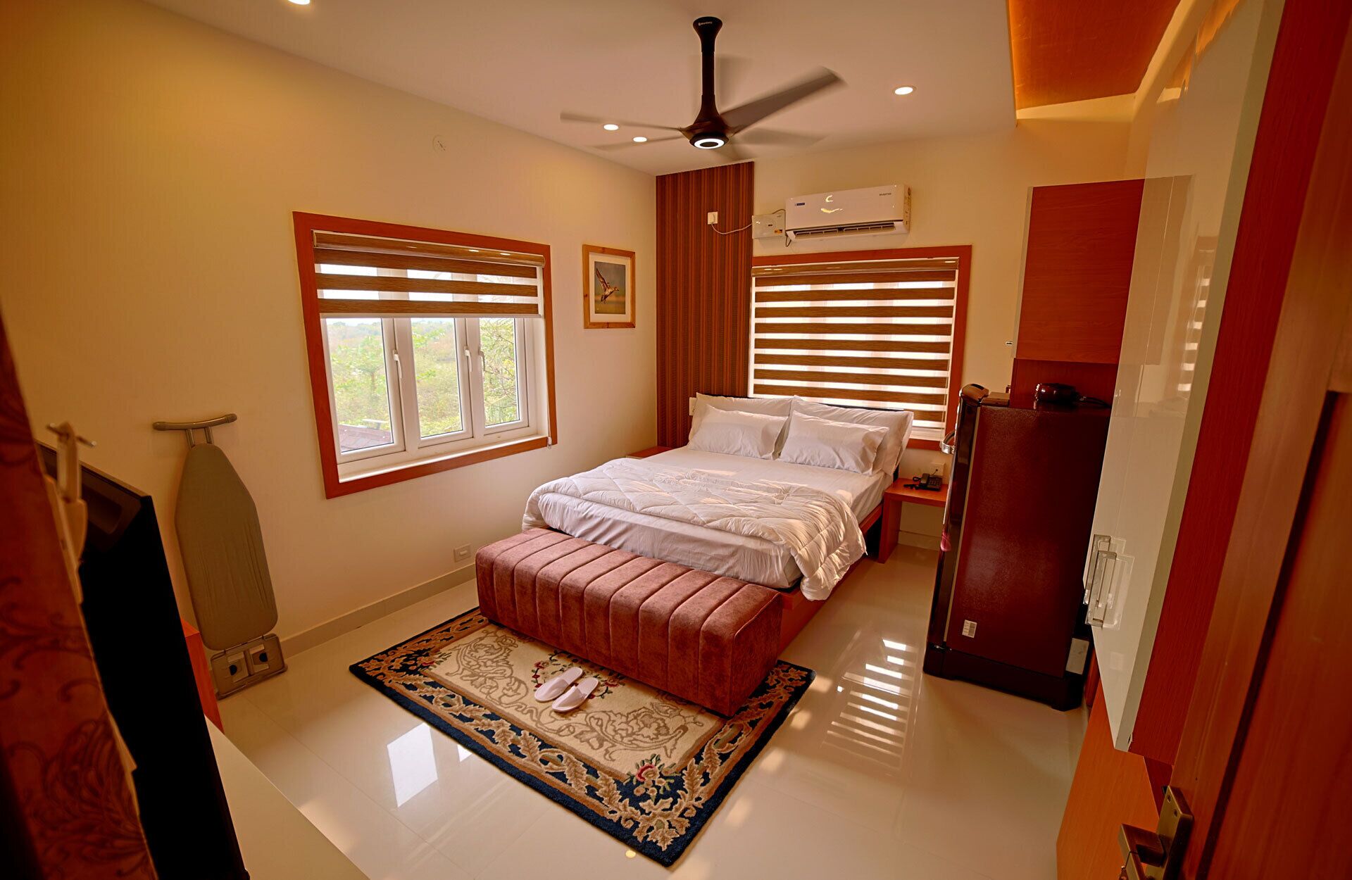 A bedroom with a bed, a ceiling fan, an air conditioning unit, and a window with blinds.