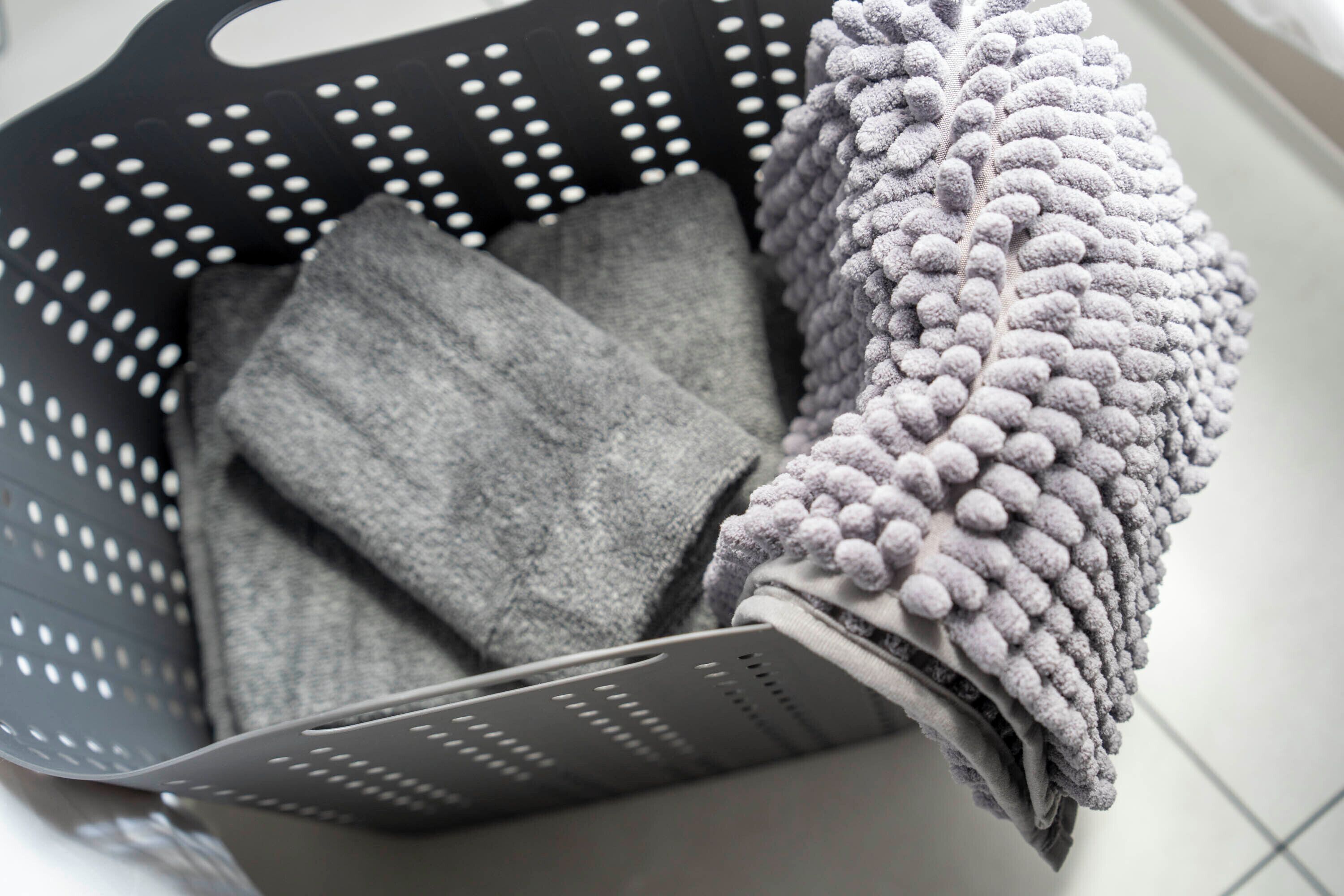 A black laundry basket with a perforated design, containing folded gray and white towels.