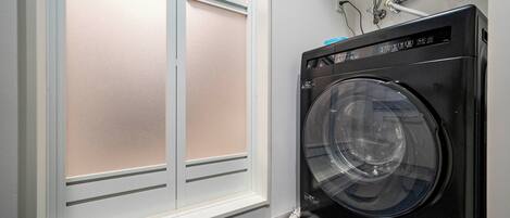 A compact, modern laundry room with a front-loading washer and dryer, a window with frosted glass, and visible plumbing.