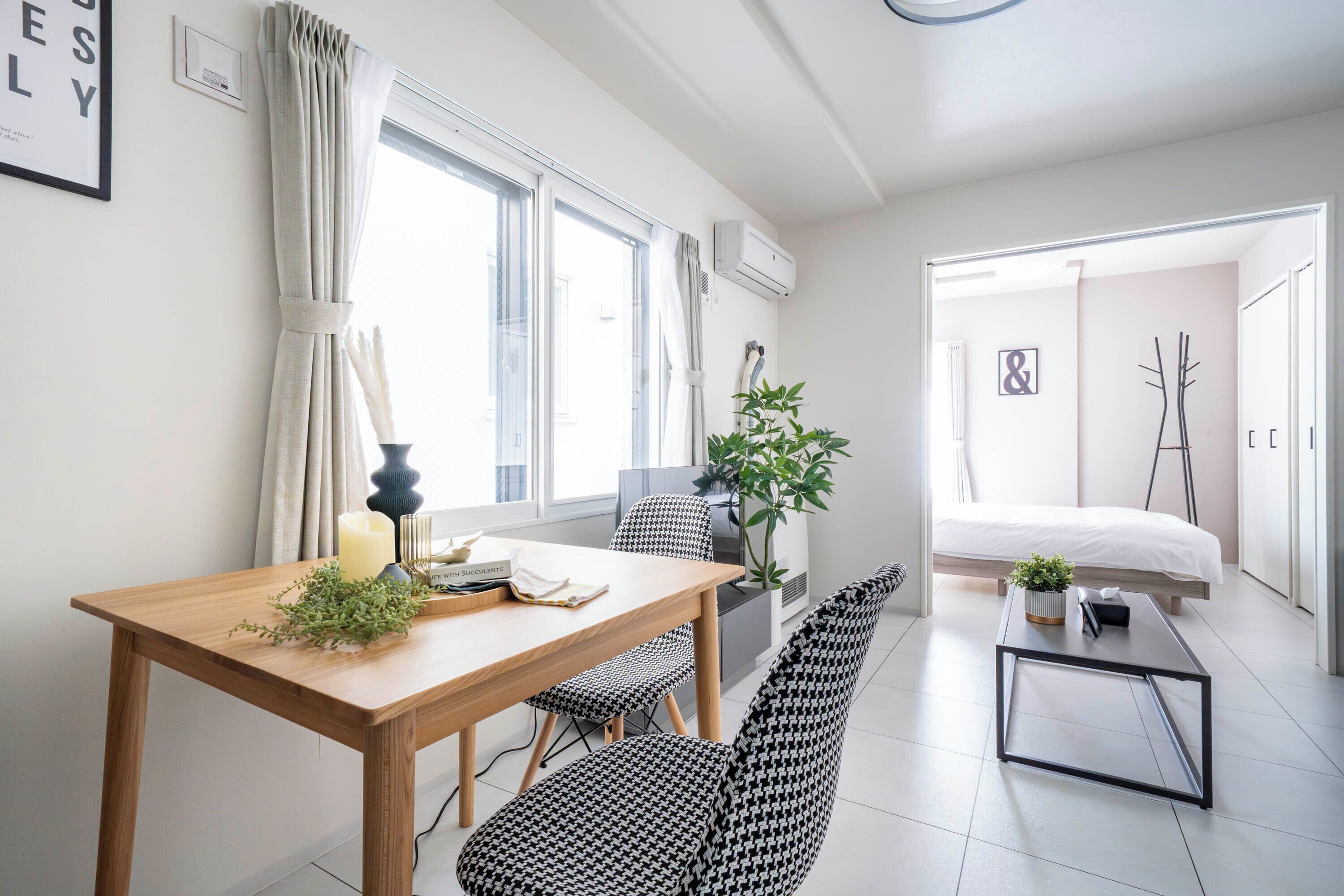 Una habitación de hotel moderna con una mesa de comedor de madera, sillas estampadas en blanco y negro, una pequeña mesa de centro negra y una cama con edredón blanco.