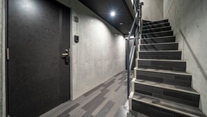 Un escalier moderne avec une rampe en métal et une porte sombre dotée d’un clavier pour l’ouverture à code.