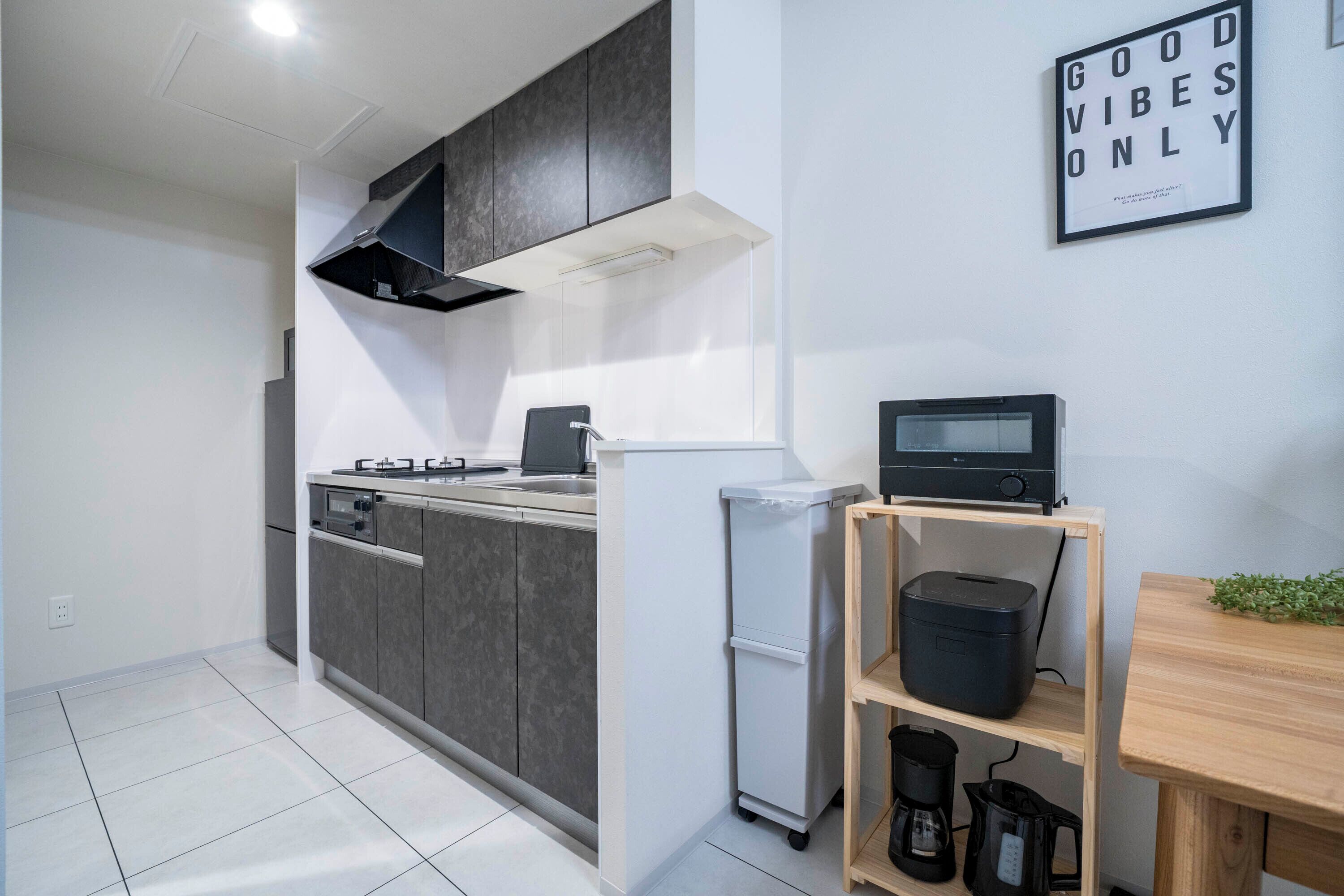 Cocina moderna con gabinetes grises, extractor de acero inoxidable, refrigerador blanco y estante de madera con electrodomésticos de cocina.